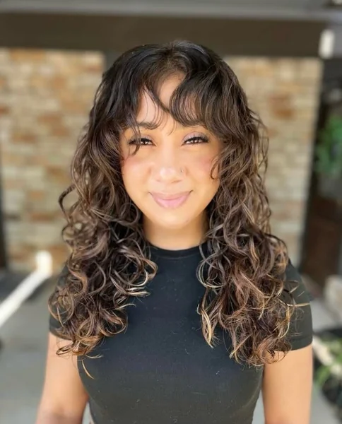 Curly Brunette Butterfly Cut with Trendy Curtain Bangs